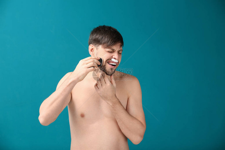 在彩色背景下使用电动剃须刀的痛苦男人图片