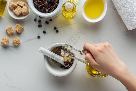 妇女将油添加到圆糖和白表面地咖啡的磅油中图片