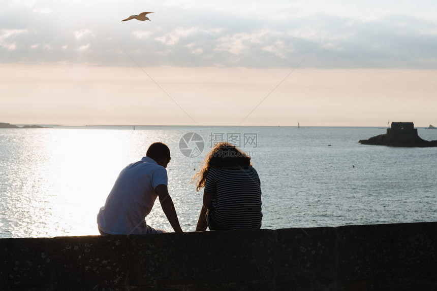 在日落时坐在墙上与大海对峙的情侣在周图片
