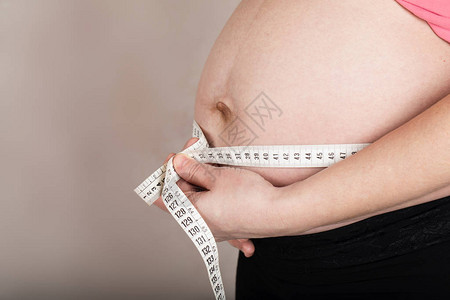 年龄在30至35岁之间的年轻怀孕妇女用测谎带测量肚子大小图片
