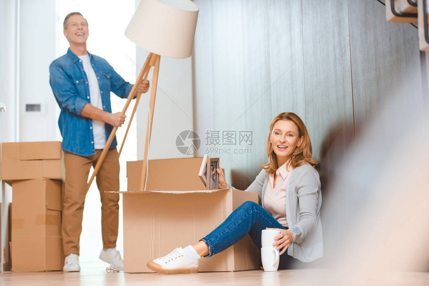 女人坐在地板上打开纸箱而丈夫拿着落地灯图片