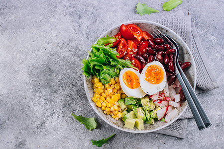 健康的素食午餐碗牛油果鸡蛋红豆番茄萝卜玉米绿叶蔬菜沙拉具体的背景顶视图片