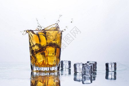 浅色背景上的冰块中的威士忌飞溅含冰威士忌或白兰地苹果汁和冷却饮料的酒图片