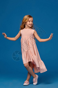 穿粉红色裙子的漂亮小女孩长着卷发穿着蓝色的背景弯曲图片