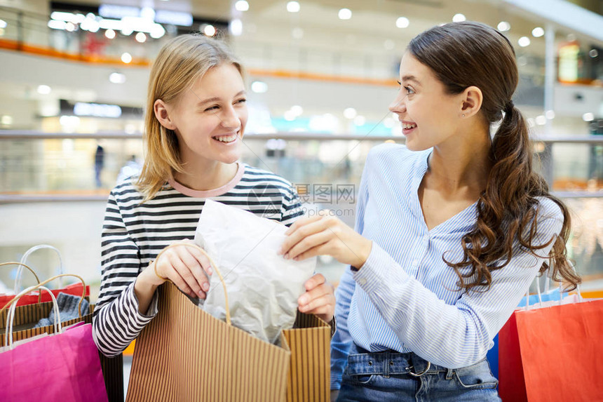 两名女孩在商场讨论购物时从纸袋中打包图片