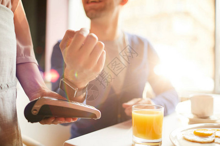 年轻人在咖啡店支付早餐时使用可穿戴支付设备的特写图片