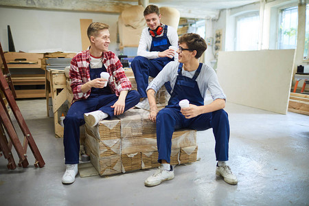 欢笑兴奋的年轻人与咖啡杯坐在包装木板上图片