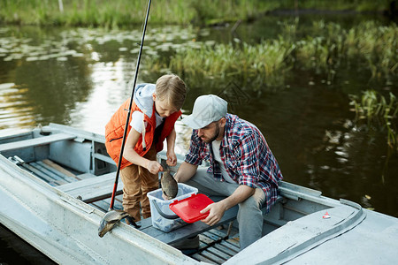 与父亲钓鱼时小男孩将大鱼放入塑图片