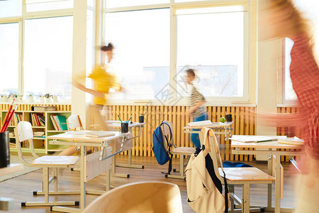 在校儿童在课堂课桌和教室内挂起背包的椅子上跑动图片