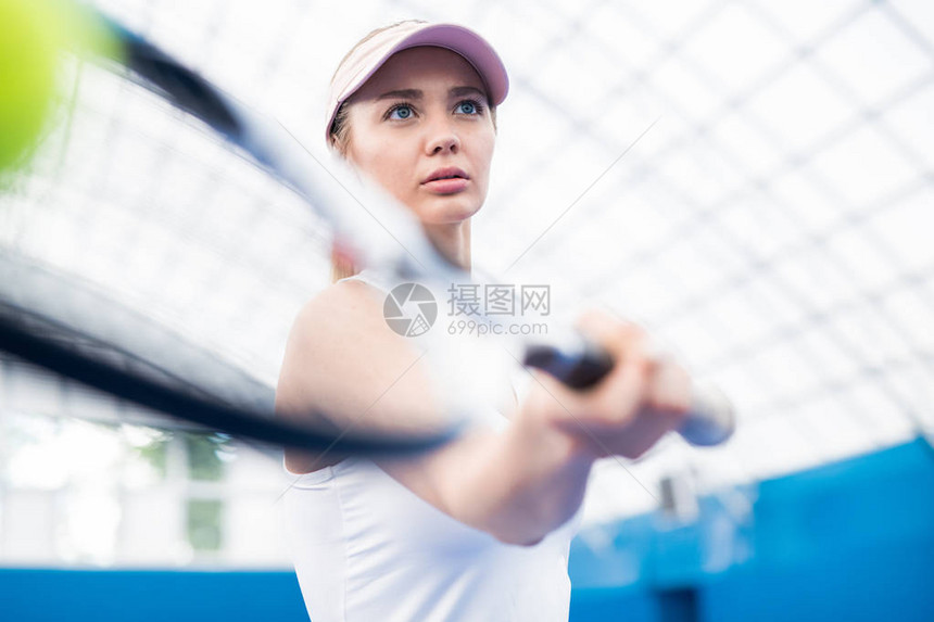 在法庭上打网球时执着的金发女金发女郎低角度肖图片