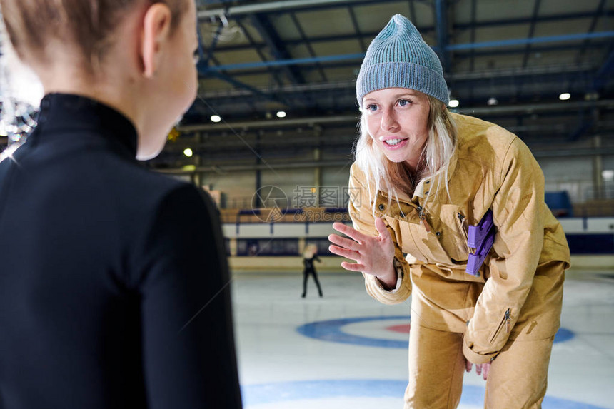 年轻女教练在室内溜冰培训中激励小女孩的肖像图片