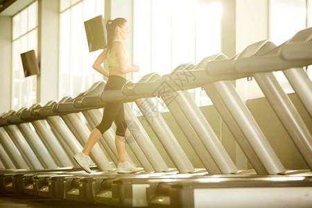 正在健身中心或健身房运动场的一支跑步机上积极穿体操练的图片
