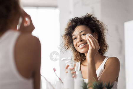 洗手间镜子前用棉垫擦脸的年轻美国女青年图片