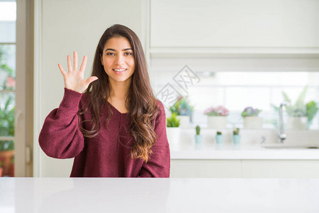 年轻漂亮的女人在家里展示并用五号手指向上指着背景图片