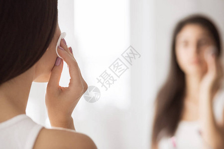 在浴室镜子前洗手间用垫子擦脸的年轻女子图片