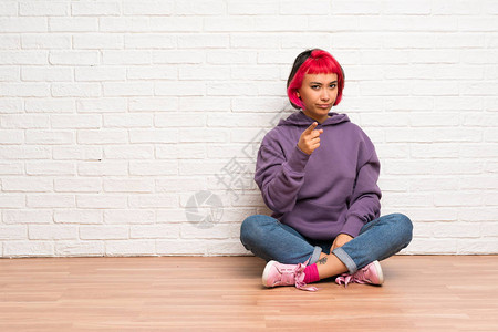 穿着粉色头发坐在地板上指着前面的年轻女图片