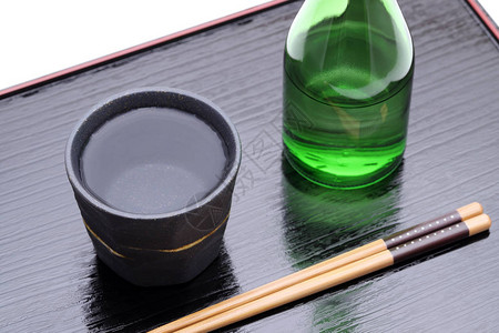 木托盘上的日本烧酒瓶和陶瓷碗白色背景图片