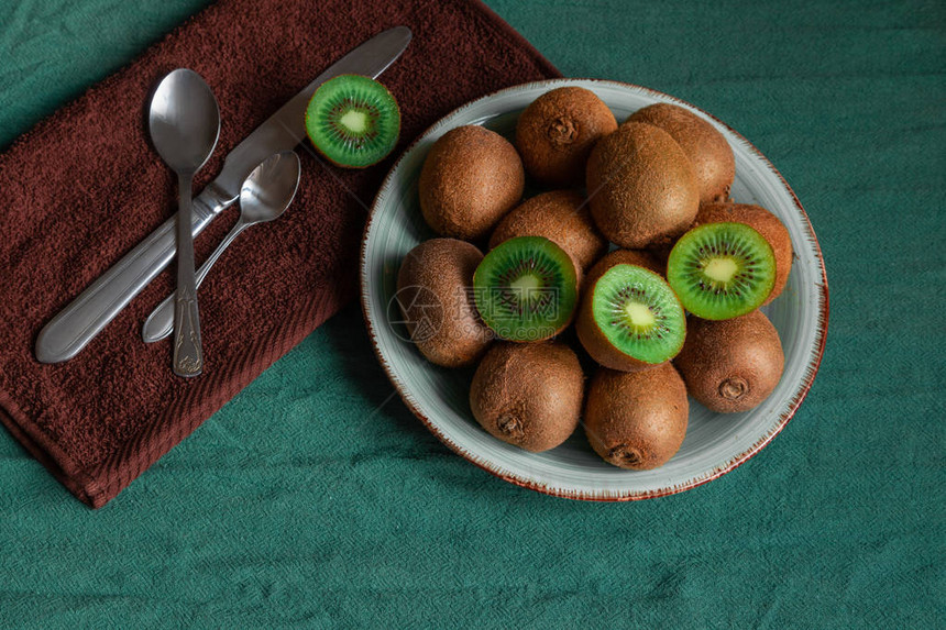绿色桌子上有很多猕猴桃餐巾勺子和刀在盘子上的健康水果猕猴桃热带水果图片