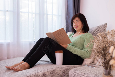 亚裔老年妇女阅读关于客厅沙发妇女生图片