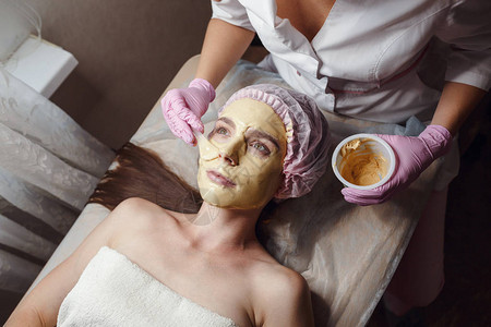 为美丽的面部皮肤剥金面膜美容师为病人做美容程序面部脱皮面膜图片