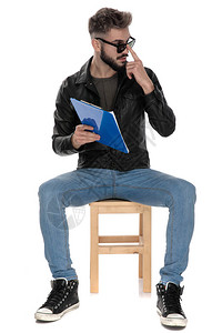 身穿黑色夹克和蓝色牛仔裤的男子坐在椅子上图片