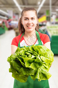 杂货店或超市女员工特写拿着表达可信的绿色生菜作为广告图片