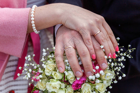 新娘和新郎手与结婚戒指以新娘花束为背景图片