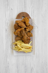 炸鸡腿辣翅炸薯条和鸡肉条在质朴的木板上图片