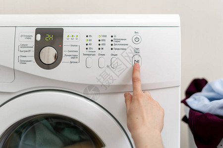 妇女用手在室内明亮公寓内白色洗衣机上选择洗衣涤器的洗衣程序图片
