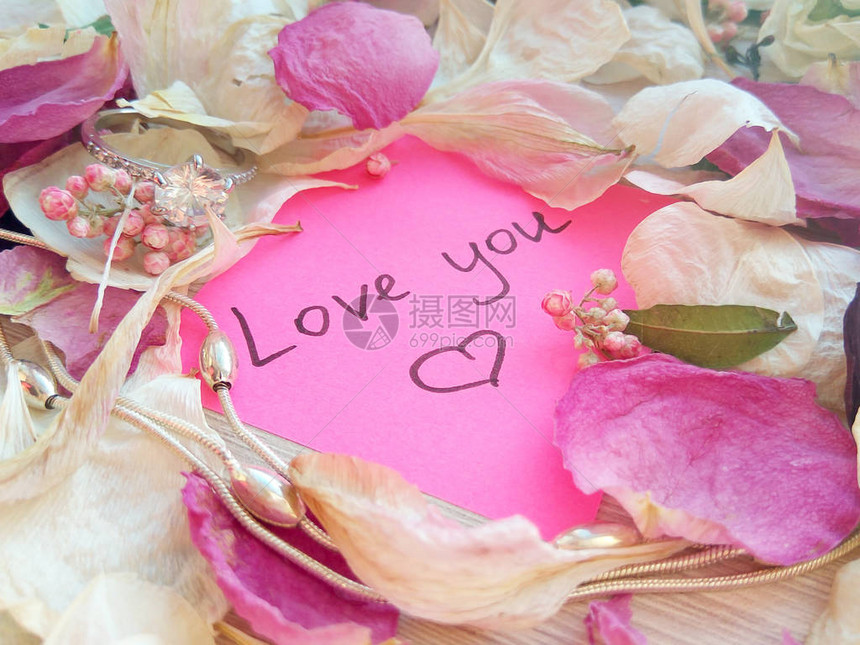 爱您在粉红粘贴纸条上的留言上面有干玫瑰兰花瓣银首饰戒指和木图片