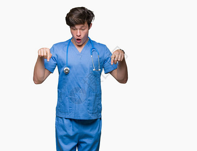 身穿医疗制服的年轻医生在孤立的背景下用手指向下指着广告惊讶的图片