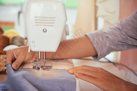 匿名时装设计师在工作室的现代缝纫机上缝制蓝色图片