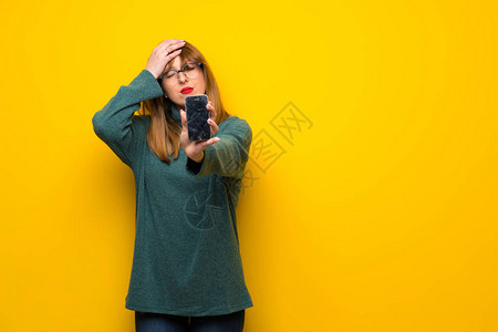 在黄色墙上戴眼镜的女人拿着破损的智能图片