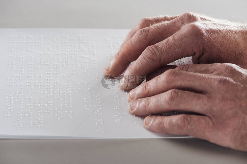 在灰色上隔开的盲文本中读取lebraille文字的高级男图片
