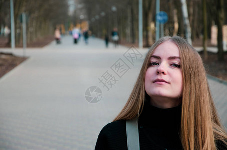 一个美丽的女孩的肖像下午穿着黑色夹克沿着公园巷子走在图片