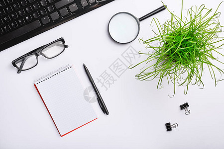 带键盘眼镜放大镜笔记本夹子办公设备和黑笔的白桌简约的工作场所平躺图片