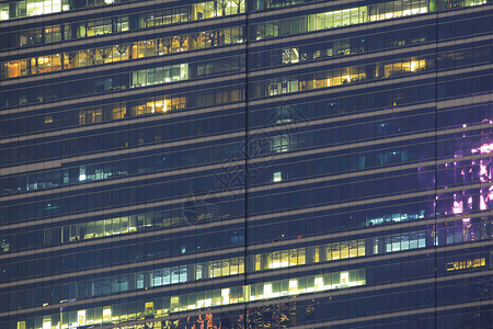 多层办公楼夜间与工人加班深夜在办公室照明和工作人员在玻璃钢和铝包覆的现代办背景图片