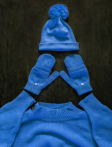 深色木质背景上带有绒球手套蓝紫青色毛衣的帽子图片