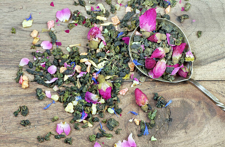 绿茶与鲜花在深色木桌上的木勺绿茶与鲜花和干果片混图片