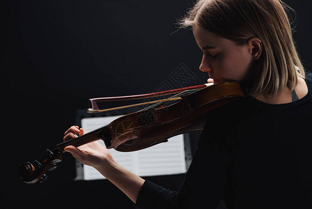 年轻女在黑暗中用大提琴和弓玩大提琴时有高清图片