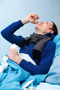 身着蓝枕头和毯子躺在床上时使用鼻喷剂的染色病棕发图片