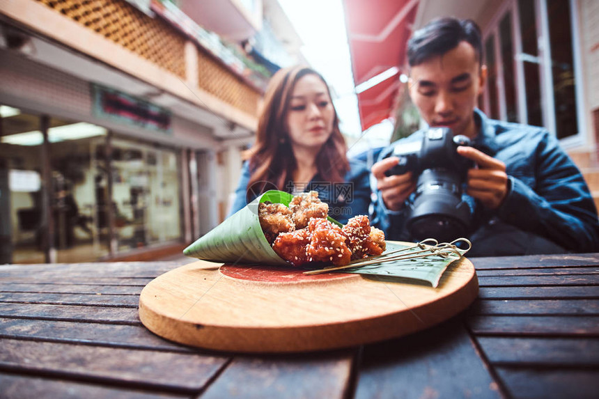 年轻的亚洲夫妇坐在外面的餐馆在木桌上的前面有传统的亚洲食物竹叶包装人们在相机上看照图片