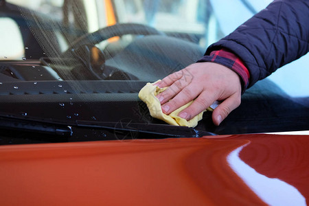 在洗车时用黄色抹布擦掉橙色汽车的挡风玻璃图片