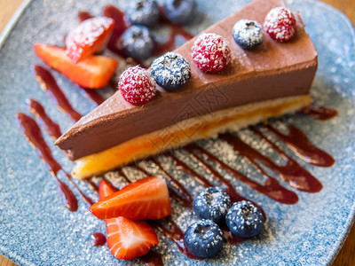 蓝盘上放着草莓蓝莓和覆盆子的巧克力芝士蛋糕图片