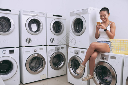 漂亮微笑的越南女人坐在洗衣房的洗衣机上图片
