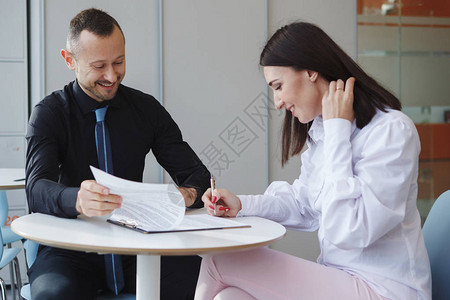 穿着黑色衬衫的商人和穿着白色衬衫的女人坐在办公室的一张桌子旁图片