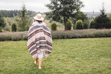 穿着雨披亚麻连衣裙和帽子的时尚髦女孩在薰衣草田里散步图片