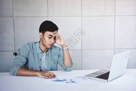 疲倦和压力的年轻商人坐在办公室的办公桌上图片