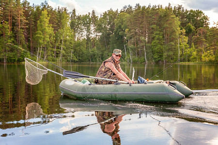 有钓鱼竿的渔夫在美丽的自然和湖泊或河流的背景下在橡皮艇上钓鱼露营旅游放松旅行积极生活背景图片