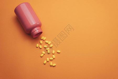 橙色背景的美丽的粉红色瓶子和黄色药图片